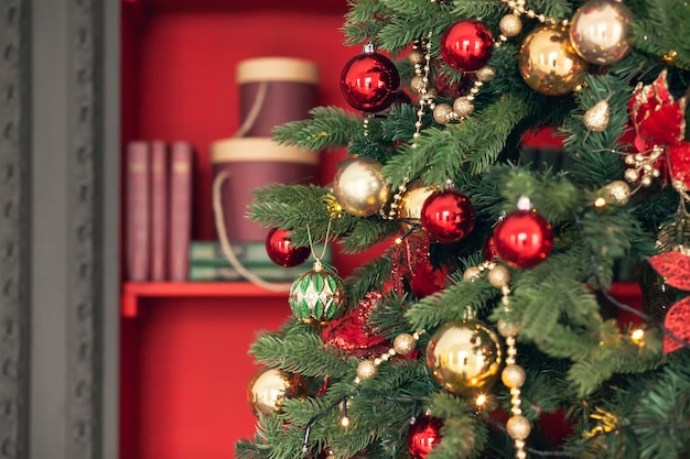 Gold and red Christmas toys, balls, garlands on a spruce branch on dark red background.