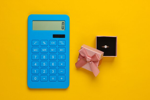 Gold ring with diamond in gift box and calculator on yellow