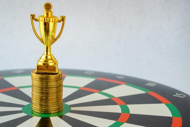 Gold trophy and stack of gold coin on dartboard hitting in the target center of dartboard Target business success and investment and finance concepts