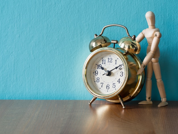 Gold vintage alarm clock on the wood table in the font of wooden puppet stand