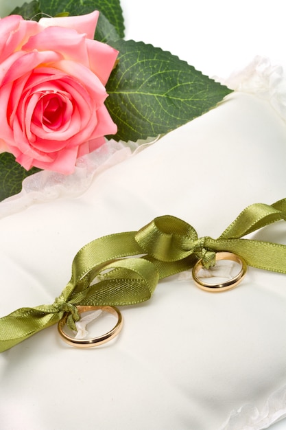 gold wedding rings on white pillow with rose