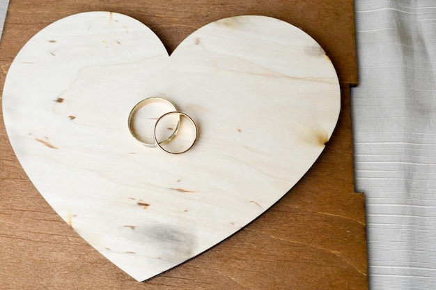 Gold wedding rings on a wooden heart Bright glittering glamorous fashionable expensive hearts