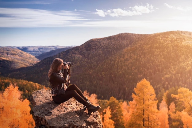 Golden autumn A young woman photographer shoots a landscape with the sky and autumn orange foliage on top of a mountain copy space freedom