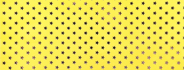 Golden background from metal foil paper with a pattern of sparkling stars closeup Texture of yellow metallized wrapping holiday backdrop