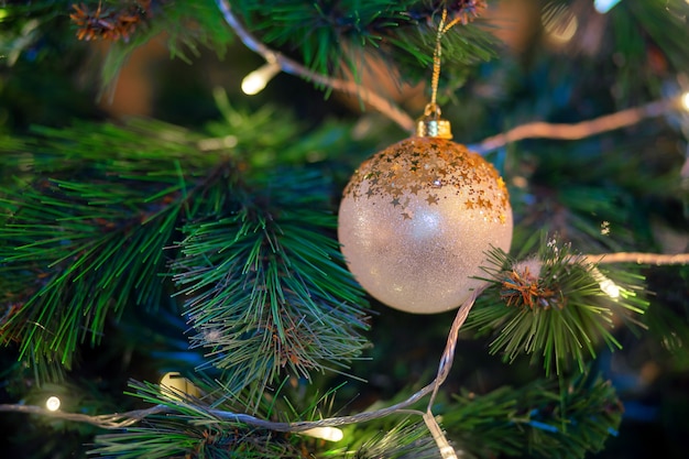 Golden ball hanging on a branch of a christmas tree. Christmas tree decoration. Preparing for the holiday, garland