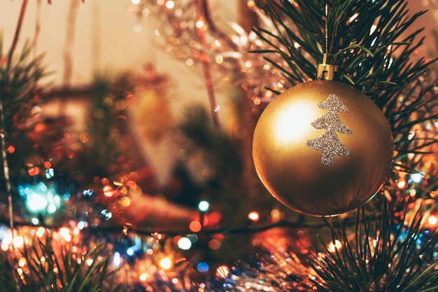 Golden ball with silver painted tree hanging on a christmas tree among the lights