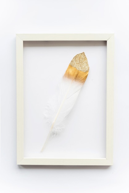 Golden bird feather in a frame on a white background with copy space for text Minimal concept View from above Easter card soft selective focus