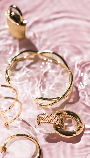 Golden bracelets earrings rings jewelery on pink water background luxury glamour and holiday beauty design for jewelry brand ads