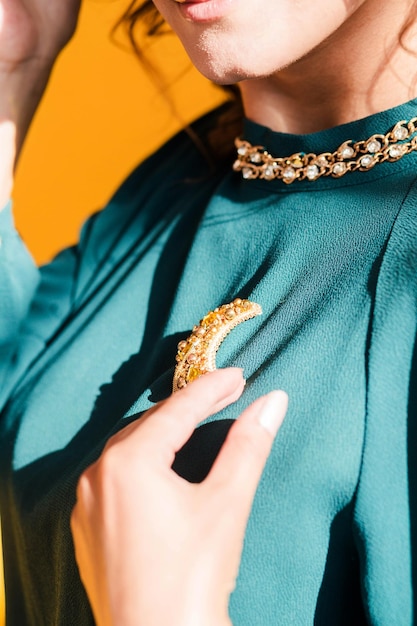 A golden brooch in the form of a month on a green blouse of a brunette girl Young woman posing on yellow background sunlight and shadow in studio