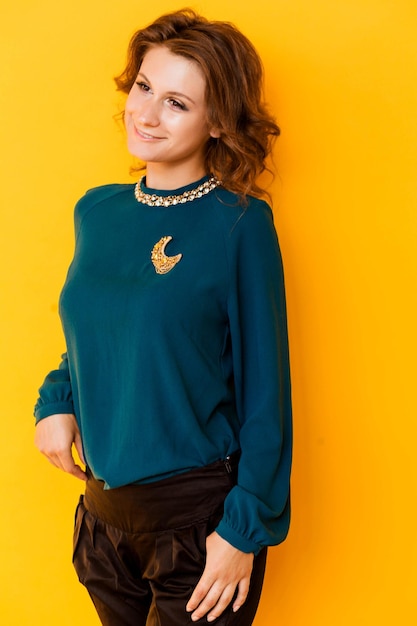 A golden brooch in the form of a month on a green blouse of a brunette girl Young woman posing on yellow background