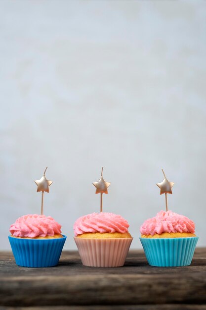 Photo golden candles in the shape of star on cupcakes with pink buttercream frosting. birthday cupcakes on wooden table. gray background. party food. vertical frame