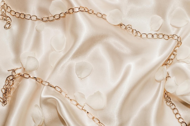 Golden chain and white petals on a silk beige background space for text