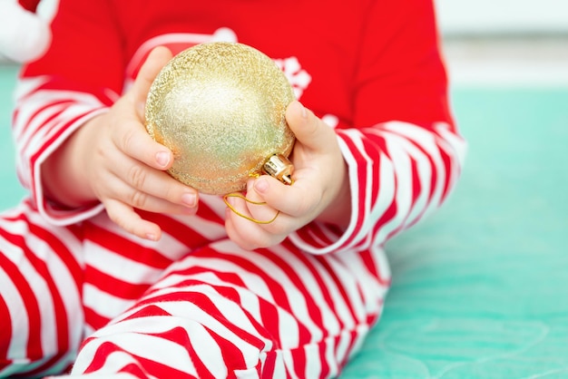 Golden christmas ball in the hands of a little baby wearing christmas costume close up new year and