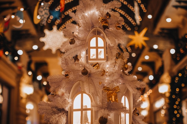 Golden Christmas balls and decorations hanging on the white Christmas tree with windows figurines