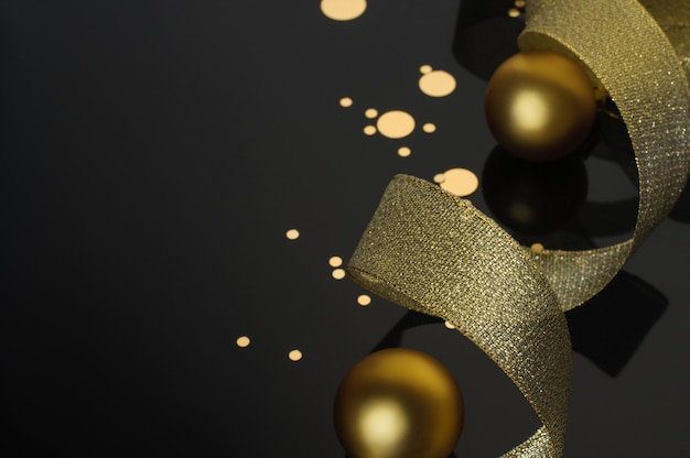 Golden christmas balls with shiny ribbon and golden candy on black background