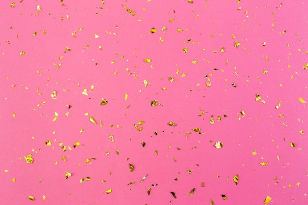 Golden confetti on pink paper background. Festive holiday backdrop. Birthday congratulations Christmas New Year. Valentines Day. Flat lay, top view, copy space.