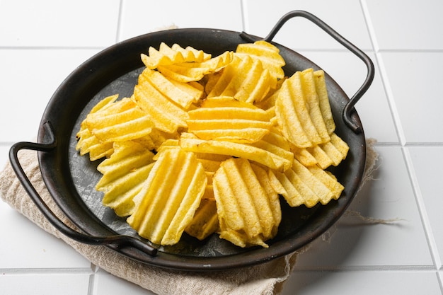 Golden corrugated potato chips on white ceramic squared tile table background