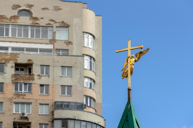 Golden cross with an angel against the blue sky and the facade of an apartment building