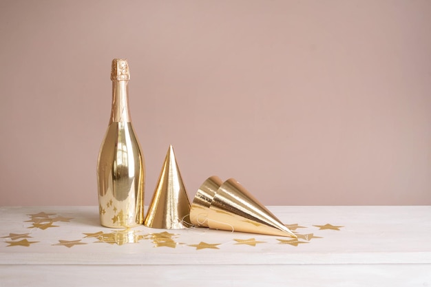 Golden festive caps and a bottle of champagne on the table Beige festive background with copy space