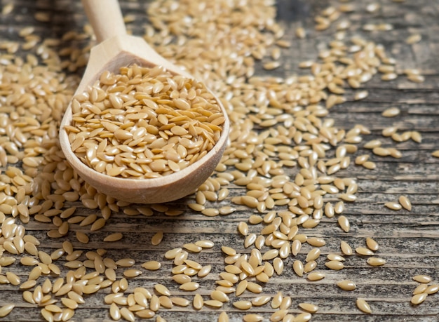 Golden flax seeds, flaxseed in a wooden spoon on an old rustic background close-up, white flax