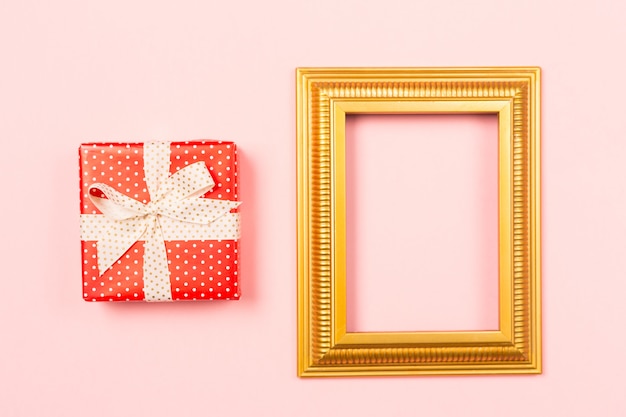 Golden frame empty blank picture and red gift box on light pink background .