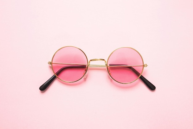 Golden frame sunglasses with pink lens on pink background top view