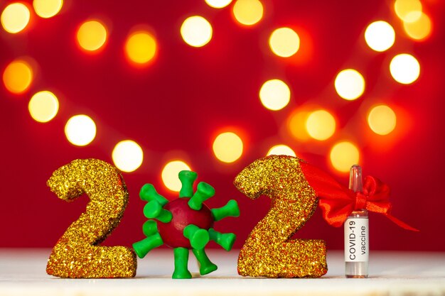 Photo golden glittering numbers 2021 with covid-19 virus and vaccine ampoule with bokeh on red background. copy space.