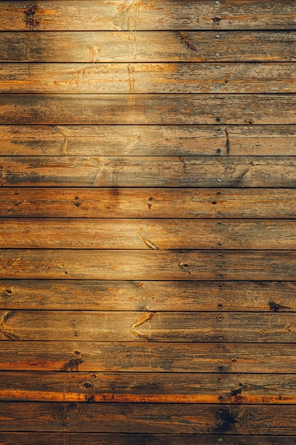 The golden hour sun casts a warm glow on the textured surface of aged wooden planks highlighting natural patterns and details