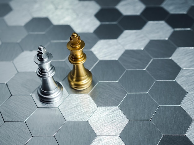 A golden king chess piece and a silver king chess piece are standing together on hexagon pattern board background Leadership partnership competitor confrontation and business strategy concept