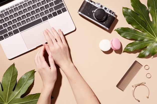 Golden laptop on beige background with green leaves. Beauty woman blog. Top view, flat lay. Home office desk.