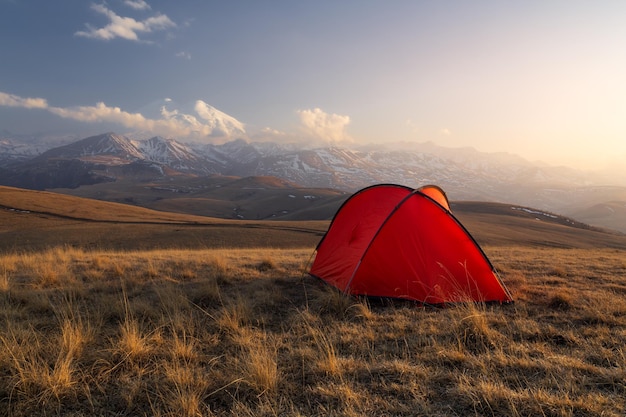 Golden light sunset with bright red tent in front of snowcovered Mount Elbrus Caucasus Russia