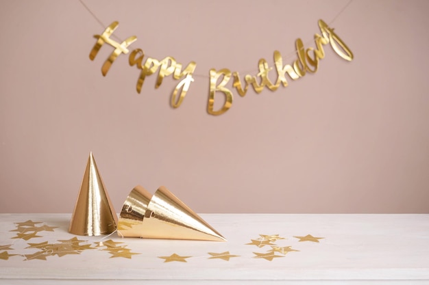 Golden party caps and an inscription happy birthday on the table Beige festive background with copy space