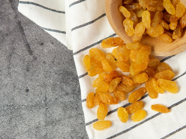 Golden raisins in a wooden bowl and a spoon on a dark concrete background Dried grapes or raisins