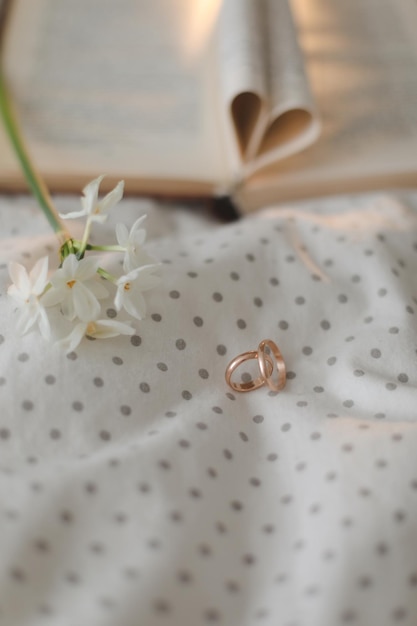 Golden ring and open book with folded sheets in heart shape in bed