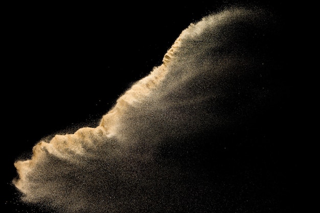 Photo golden sand explosion isolated on black background. abstract sand cloud.