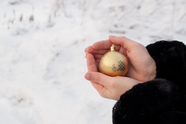 A golden shiny ball in women's hands on a winter blurry background