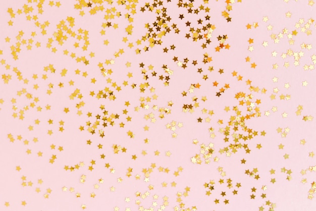 Golden star glitter confetti on pale pink background. Top view, flat lay.