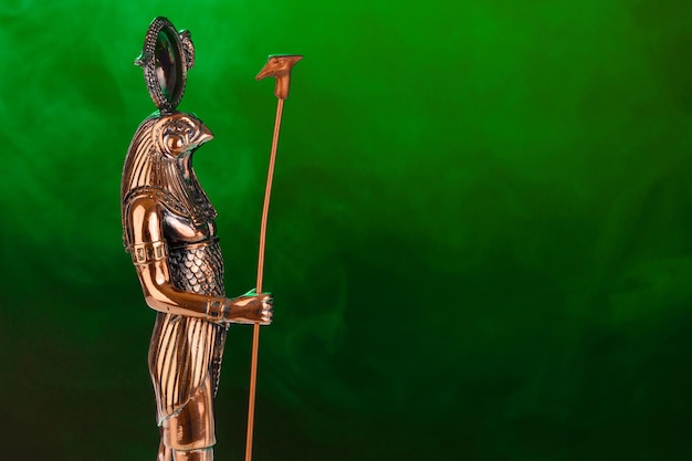 Golden statue of the Egyptian god Ra with the head of a falcon on a black background with green illumination