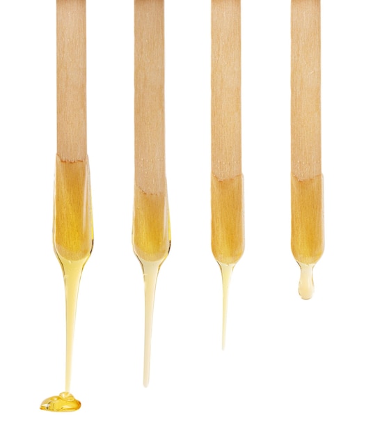 Golden sugar paste or wax for depilation dripping from wooden stick isolated on white background