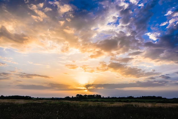 Golden sunrise or sunset in the cloudy sky with sun rays in summer over the meadow