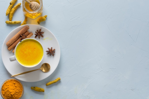 Golden turmeric milk with honey and ingredients on blue.