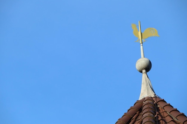 Photo a golden weather vane stands out on a rooftop against the backdrop of a clear blue sky