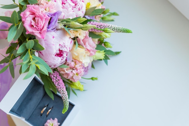 Golden wedding rings on bridal bouquet with fresh flowers rice flower pink peonies eustoma Marriage eternal love concept Top view close upstylish golden rings in a white box