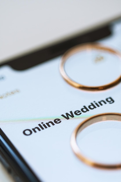 Golden wedding rings on top of a smartphone and the text on the screen Online Wedding