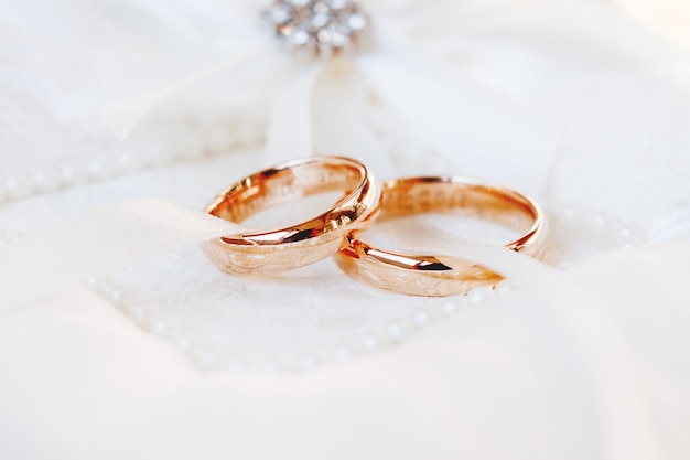 Golden wedding rings on white silk background. Wedding details. Symbol of love and marriage.