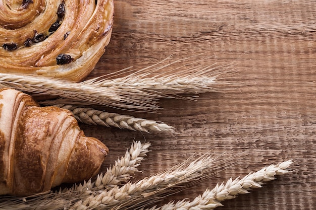 Golden wheat ears roll with raisins baked croissant on oaken wooden board food and drink concept