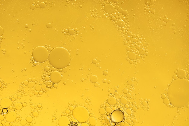 Golden yellow abstract oil bubbles or face serum background. Oil and water bubbles macro photography