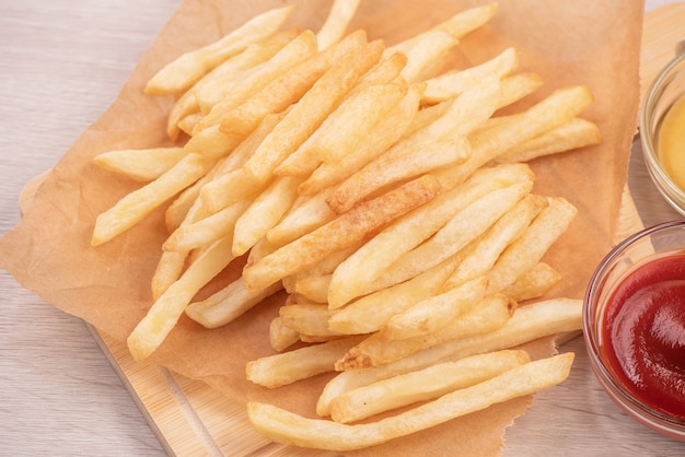 Golden yummy deep French fries on kraft baking sheet paper and serving tray to eat with ketchup and yellow mustard, close up, lifestyle.