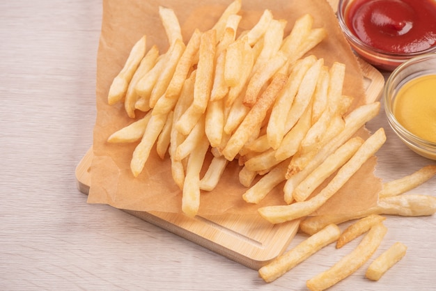 Golden yummy deep French fries on kraft baking sheet paper and serving tray to eat with ketchup and yellow mustard, top view, lifestyle.