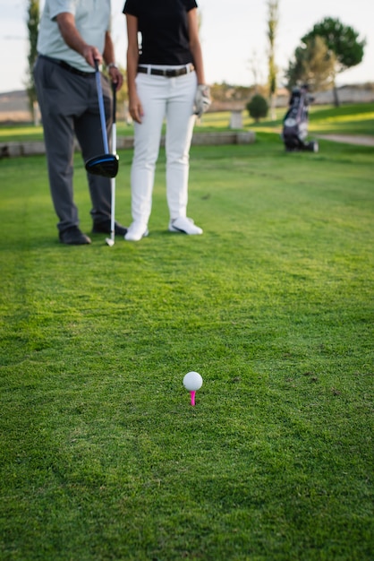 golf ball resting on the tee with two players out of focus in the background. Tee box on golf course.